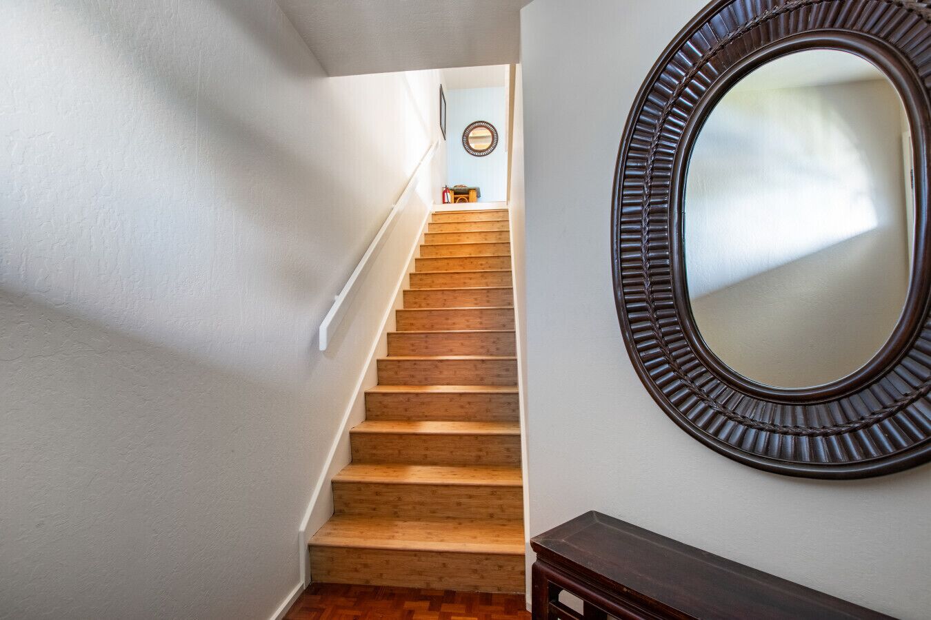 Un escalier en bois, avec des murs blancs et un grand miroir doté d’un cadre décoratif.
