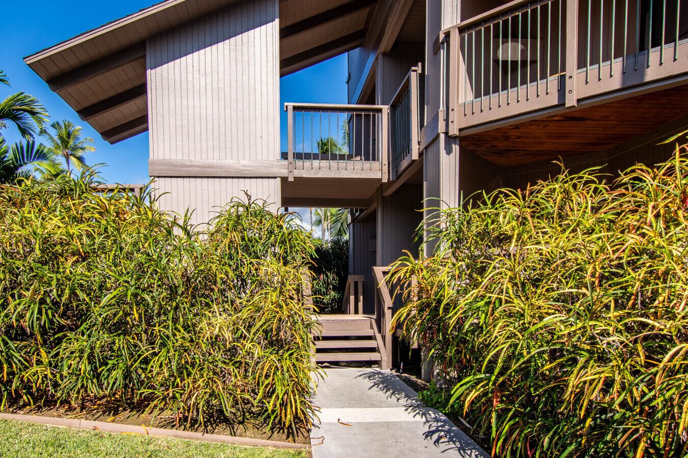 A modern building with a concrete exterior, a wooden deck, and a staircase leading to a balcony.