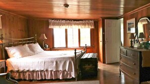 A wooden-paneled bedroom with a bed, dresser, and a window with curtains.