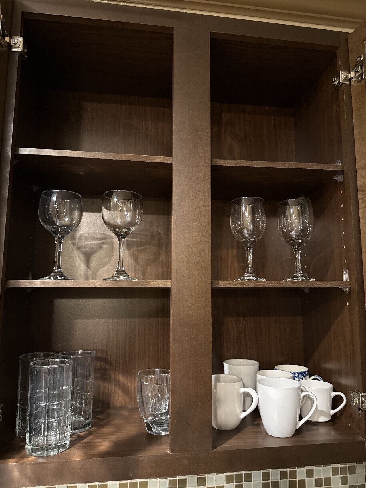 A wooden cabinet with shelves holding wine glasses and white mugs.