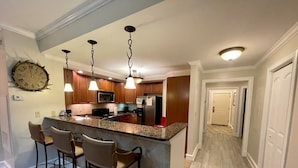 A modern kitchen with a granite countertop, wooden cabinets, and a built-in island with bar stools.