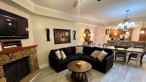 A living room with a fireplace, black sectional sofa, and a dining area with a chandelier.