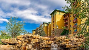 A multi-story hotel with balconies, a stone waterfall feature, and a clear sky.
