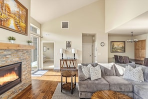 A living room with a fireplace, a gray sofa, a dining area, and a hallway leading to another room.