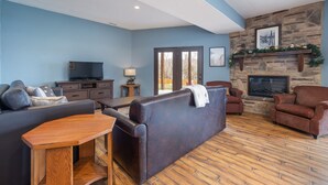 A modern living room with a stone fireplace, a flat-screen TV, and a dining area. - Gorgeous 10 Bedroom Lakefront Lodge (Branson)