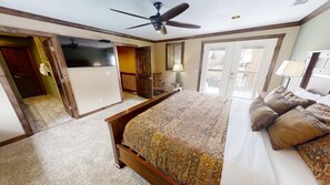 A bedroom with a large bed, a ceiling fan, a sliding door to a balcony, and a view of the outdoors.