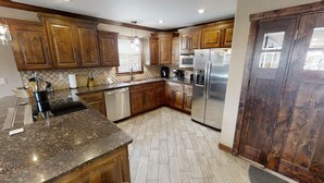 Une cuisine dotée de meubles en bois, de plans de travail en granit, d’appareils électroménagers en acier inoxydable et d’un dosseret décoré d’un motif en chevrons.