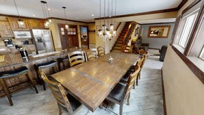 Un vaste espace de salle à manger avec une grande table et des chaises en bois, une cuisine équipée d’appareils électroménagers modernes et un escalier menant à un niveau supérieur.