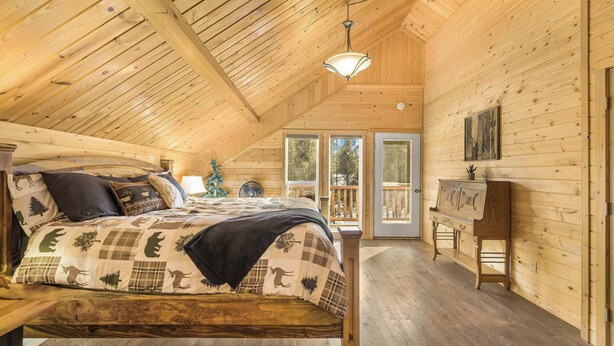 Une chambre dans une cabane en bois, avec un lit, un banc et une vue sur l’extérieur.