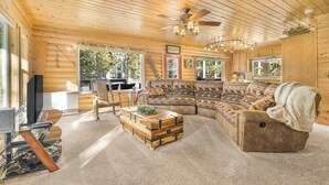 L’intérieur d’une cabane en rondins, avec un grand plafond en bois, un canapé d’angle, une table basse en bois et un téléviseur.