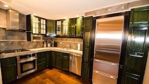 Een moderne keuken met donkergroene kastjes, roestvrijstalen apparatuur en een houten vloer.