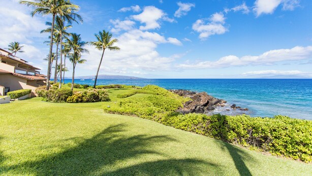 A well-maintained lawn, palm trees, and a view of the ocean. - Makena Surf • Bright and Airy Retreat • Steps to the Beach: Swim w/Turtles (Kihei)