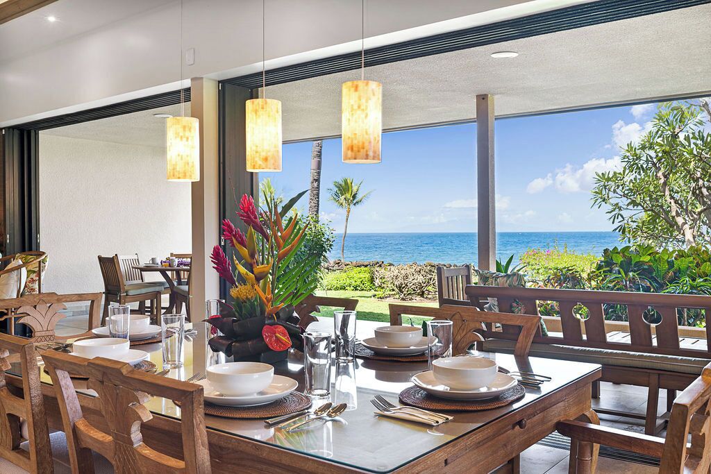A dining area with a view of the ocean, wooden furniture, and hanging pendant lights.