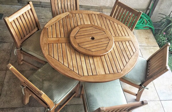 A round wooden table with a central cut-out surrounded by six wooden chairs with cushioned seats. - Makena Surf • Bright and Airy Retreat • Steps to the Beach: Swim w/Turtles (Kihei)