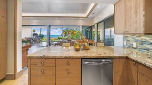 A modern kitchen with wooden cabinets, granite countertops, and a dishwasher. - Makena Surf • Bright and Airy Retreat • Steps to the Beach: Swim w/Turtles (Kihei)