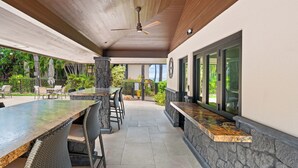 An outdoor patio with a stone wall, a wooden ceiling, and a ceiling fan. - Makena Surf • Bright and Airy Retreat • Steps to the Beach: Swim w/Turtles (Kihei)