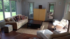 A living room with a sofa, coffee table, ottoman, and a cabinet. There are large windows and a door leading outside. - Unique home five minutes from Miami University (Oxford)