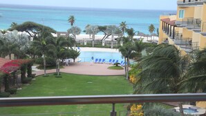 A pool area with lounge chairs, palm trees, and a view of the ocean. - 2 Bedroom, Beachfront, Amazing Ocean View, Modern ful (Eagle Beach)
