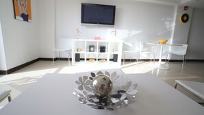 A modern living room with a white sofa, a coffee table with a decorative glass top, a flat-screen TV mounted on the wall, and a white entertainment unit with various items. - 2 Bedroom, Beachfront, Amazing Ocean View, Modern ful (Eagle Beach)