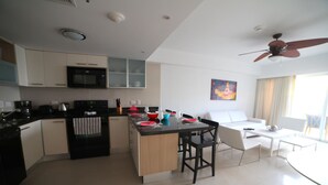 A modern kitchen with a central island, white cabinetry, and a dining area with a white sofa and chairs. - 2 Bedroom, Beachfront, Amazing Ocean View, Modern ful (Eagle Beach)