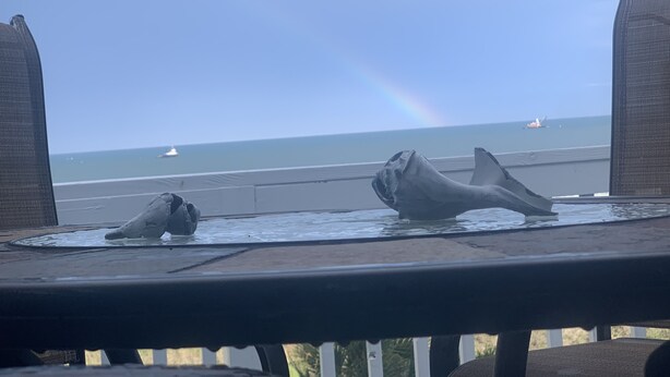 Blick auf das Meer mit einem Regenbogen, zwei Wal-Skulpturen und einem Boot in der Ferne.
