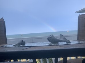 Une vue sur l’océan, avec un arc-en-ciel, deux statues de baleines et un bateau au loin.