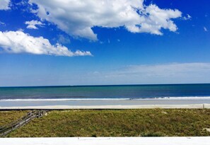 A beach with a wooden boardwalk leading to the shore, a clear sky, and calm ocean waters.