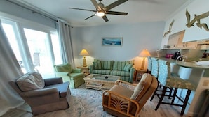 Ein Wohnzimmer mit Deckenventilator, einem grünen Sofa, einem braunen Sessel und einem Couchtisch.