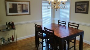 A dining room with a wooden table, four chairs, a chandelier, and a wine rack with bottles.