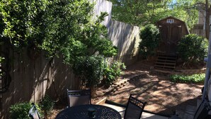A patio area with a round table and chairs, surrounded by a wooden fence and greenery.