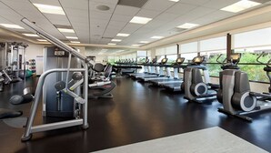 Ein Fitnessstudio mit verschiedenen Trainingsgeräten, darunter Laufbänder und Kraftgeräte, in einem großzügigen Raum mit großen Fenstern für natürliches Licht.
