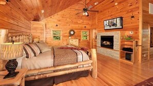 Un dormitorio tipo cabaña de madera con una cama de madera, chimenea y ventilador de techo.
