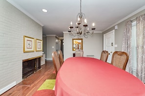 A dining area with a large table, chairs, a chandelier, a fireplace, and framed pictures on the wall.