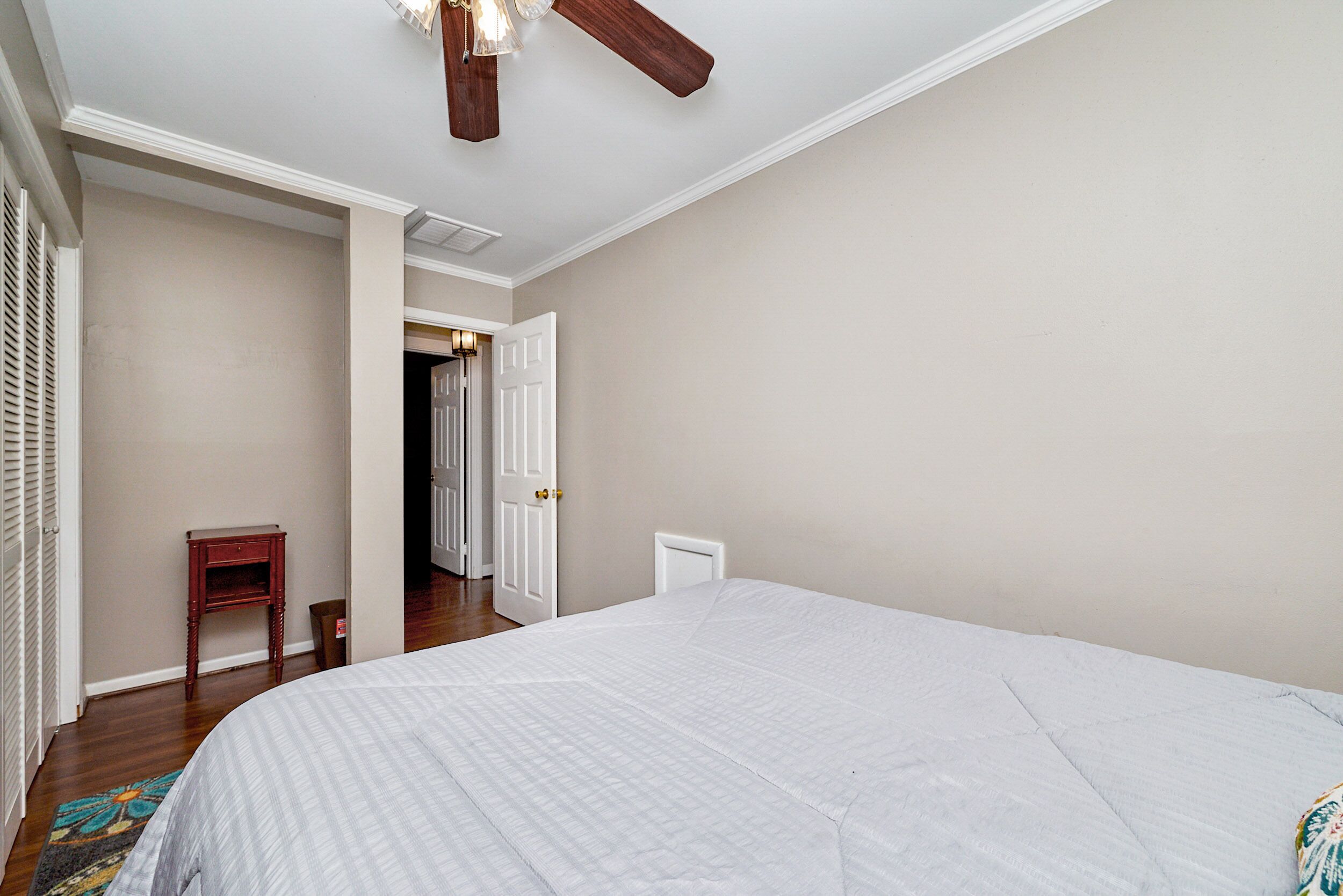 Une chambre à coucher avec un grand lit, une tête de lit en bois, un ventilateur de plafond et une porte donnant sur une autre pièce.