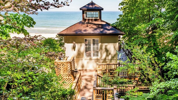 A wooden structure with a small tower, surrounded by lush greenery and overlooking a beach. - 2024 remodeled historic Lake Michigan waterfront Union Pier home with spa. (Chikaming Township)