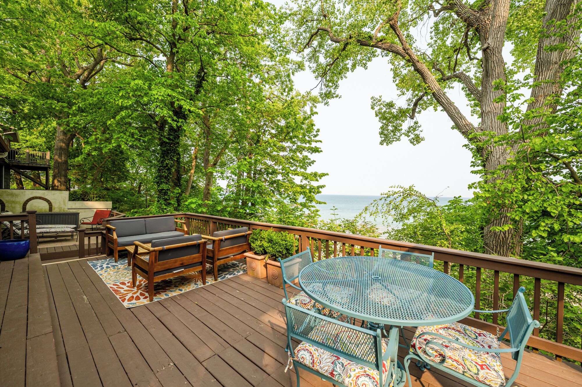 A wooden deck with outdoor furniture, including a sofa, chairs, and a table, overlooking a body of water.