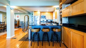 A modern kitchen with wooden cabinets, a black countertop, and three stools. - 2024 remodeled historic Lake Michigan waterfront Union Pier home with spa. (Chikaming Township)