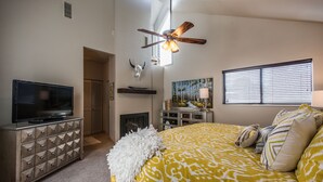 A bedroom with a bed, a TV, a fireplace, a ceiling fan, and a window with blinds. - Luxurious and modern townhome with a ton of room! (Park City)