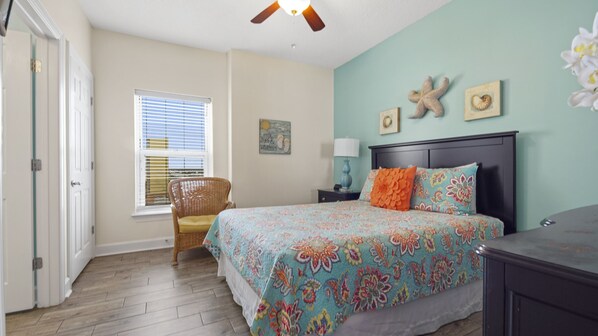 A bedroom with a bed, a chair, a nightstand, and a window with blinds. - Emerald Isle 1401 - Front row beach chair service included! Affordable rates! (Panama City Beach)