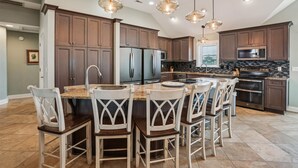 Una cocina amplia con armarios de madera oscura, una isla central con taburetes de bar, electrodomésticos de acero inoxidable e iluminación colgante.