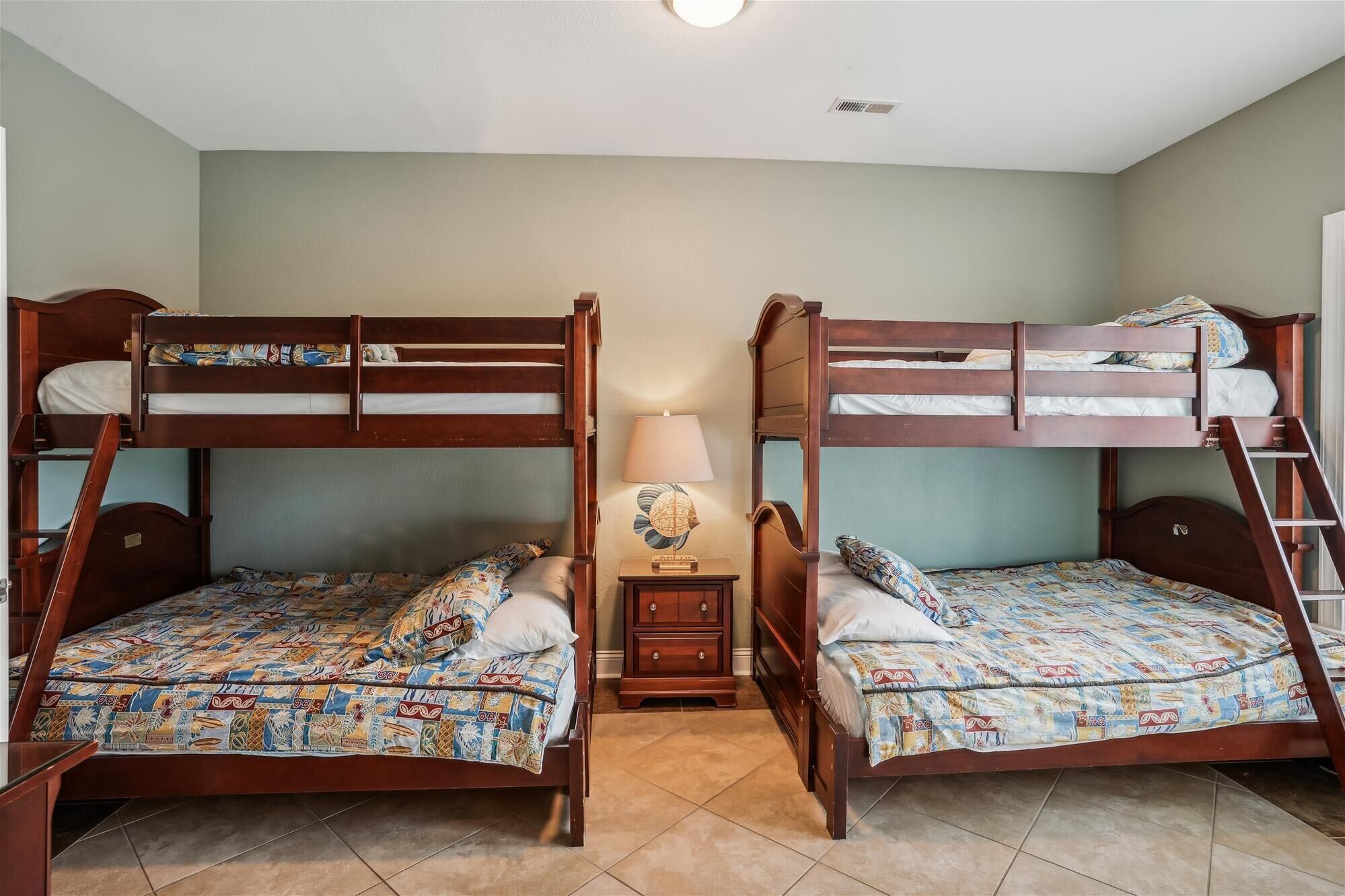 A room with two bunk beds, a small bedside table with a lamp, and a tiled floor.
