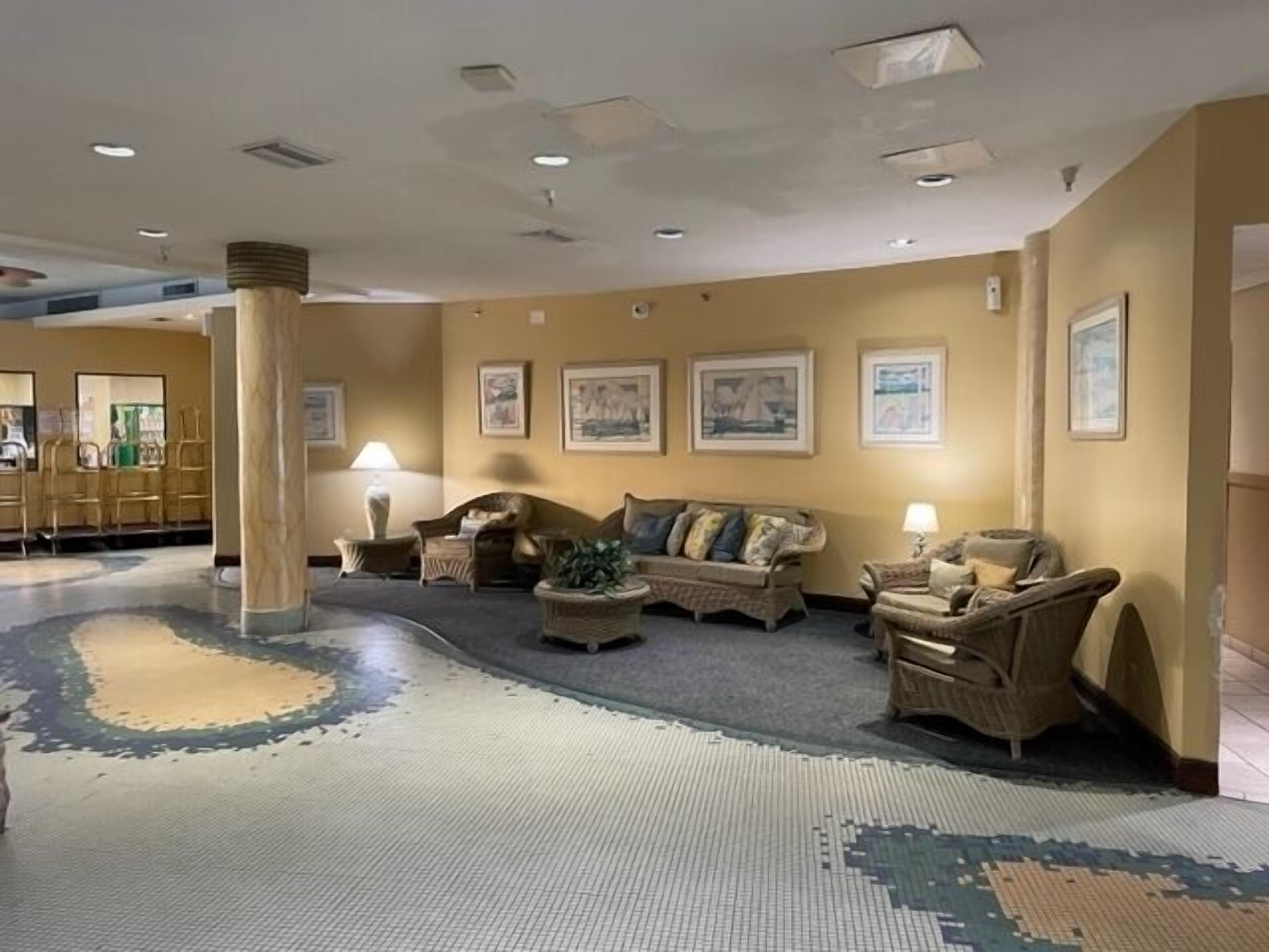 En lobby med et opholdsområde med sofaer og lænestole, et gulvtæppe med et mønster, og indrammede kunstværker på væggene.