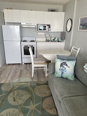 A compact kitchen with a refrigerator, stove, microwave, and a dining area with a table and chairs.