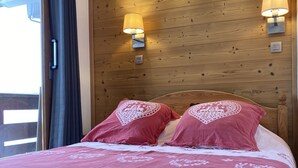 A bedroom with a wooden headboard, two bedside lamps, and a bed with pink bedding and decorative pillows. - Apartment ,Direct access to the slopes,4-6 persons,35 m2,beautiful view,wifi (Les Allues)