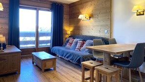 A cozy room with a wooden ceiling, a sofa with patterned cushions, a dining table with chairs, and a small wooden stool. - Apartment ,Direct access to the slopes,4-6 persons,35 m2,beautiful view,wifi (Les Allues)