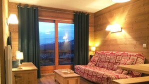 A cozy room with a wooden interior, a sofa with patterned cushions, a small wooden table, and a view through a glass door. - Apartment ,Direct access to the slopes,4-6 persons,35 m2,beautiful view,wifi (Les Allues)