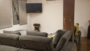 Ein Wohnzimmer mit grauem Sofa, einem flachbildfernseher an der Wand und einem kleinen Beistelltisch.