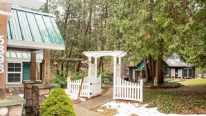 Uma casa de pedra com telhado verde, cerca branca de piquete e pérgola de madeira.