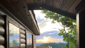 Eine Holzterrasse mit Blick auf einen Sonnenuntergang und eine bewaldete Landschaft.
