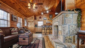 Ein gemütliches Blockhaus-Interieur mit Kamin aus Stein, Holzwänden, einer Ledersofa und einem Essbereich.